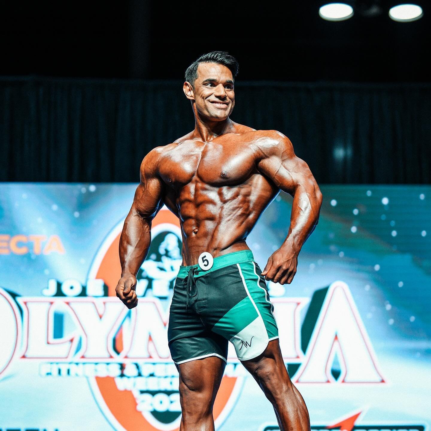 Ali Bilal on the Mr. Olympia stage in green and black board shorts