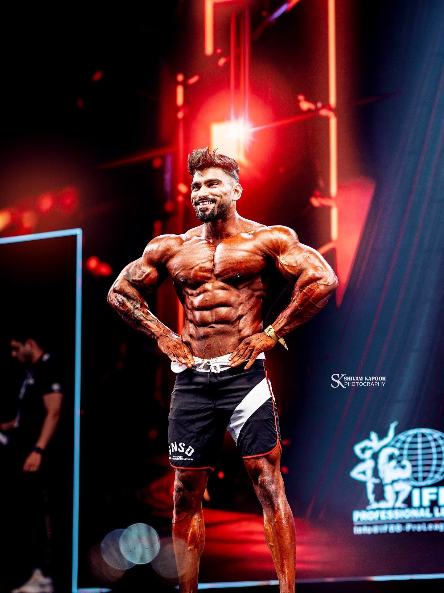 Amit Agre posing on an IFBB Pro League stage in India, hands on hips and smiling