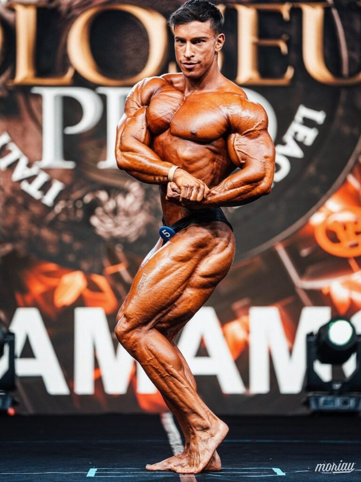 Andrea Mammoli hitting a side chest pose on stage at the Koloseum Pro in Italy