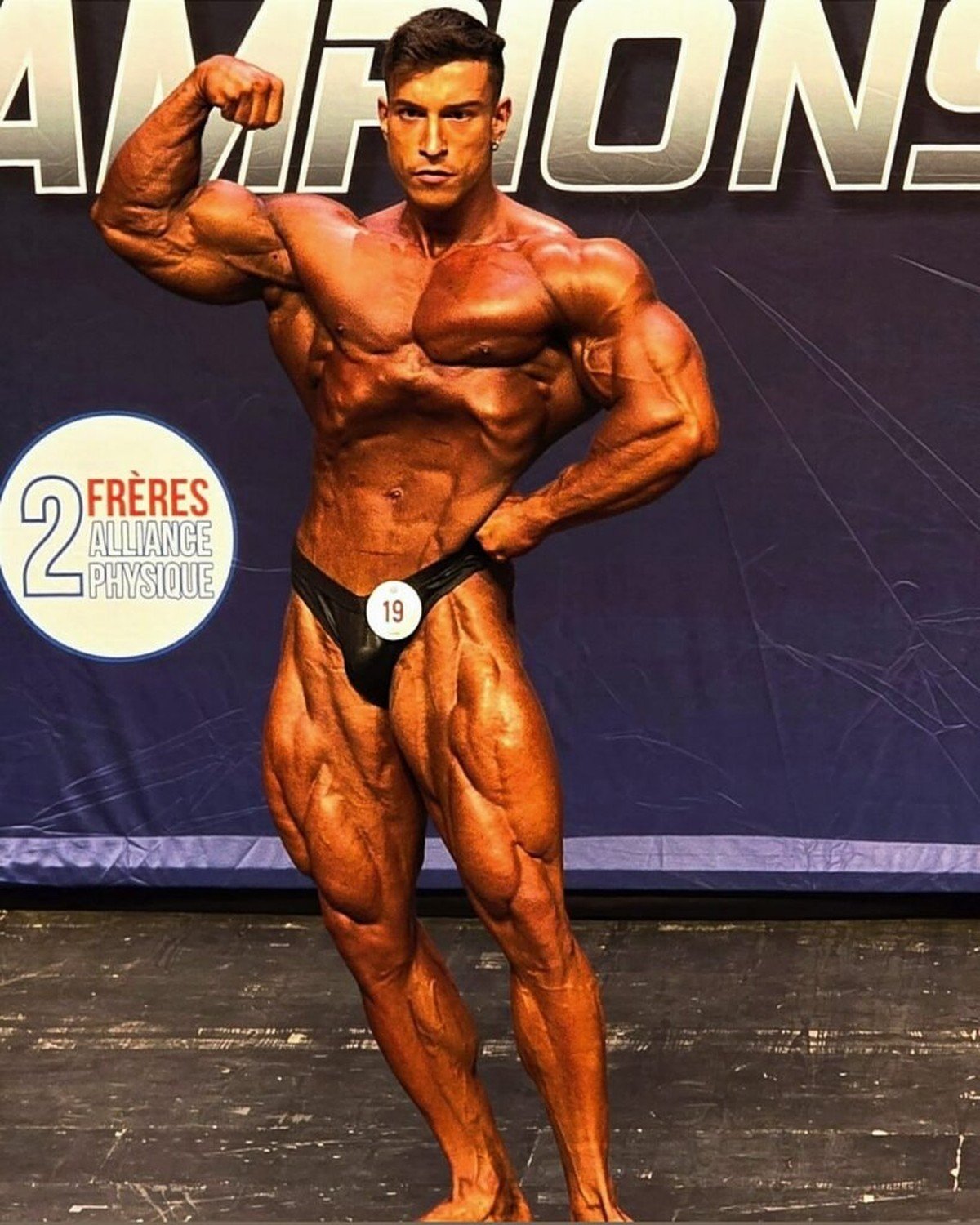 Andrea Mammoli posing on stage in France wearing competitor number 19