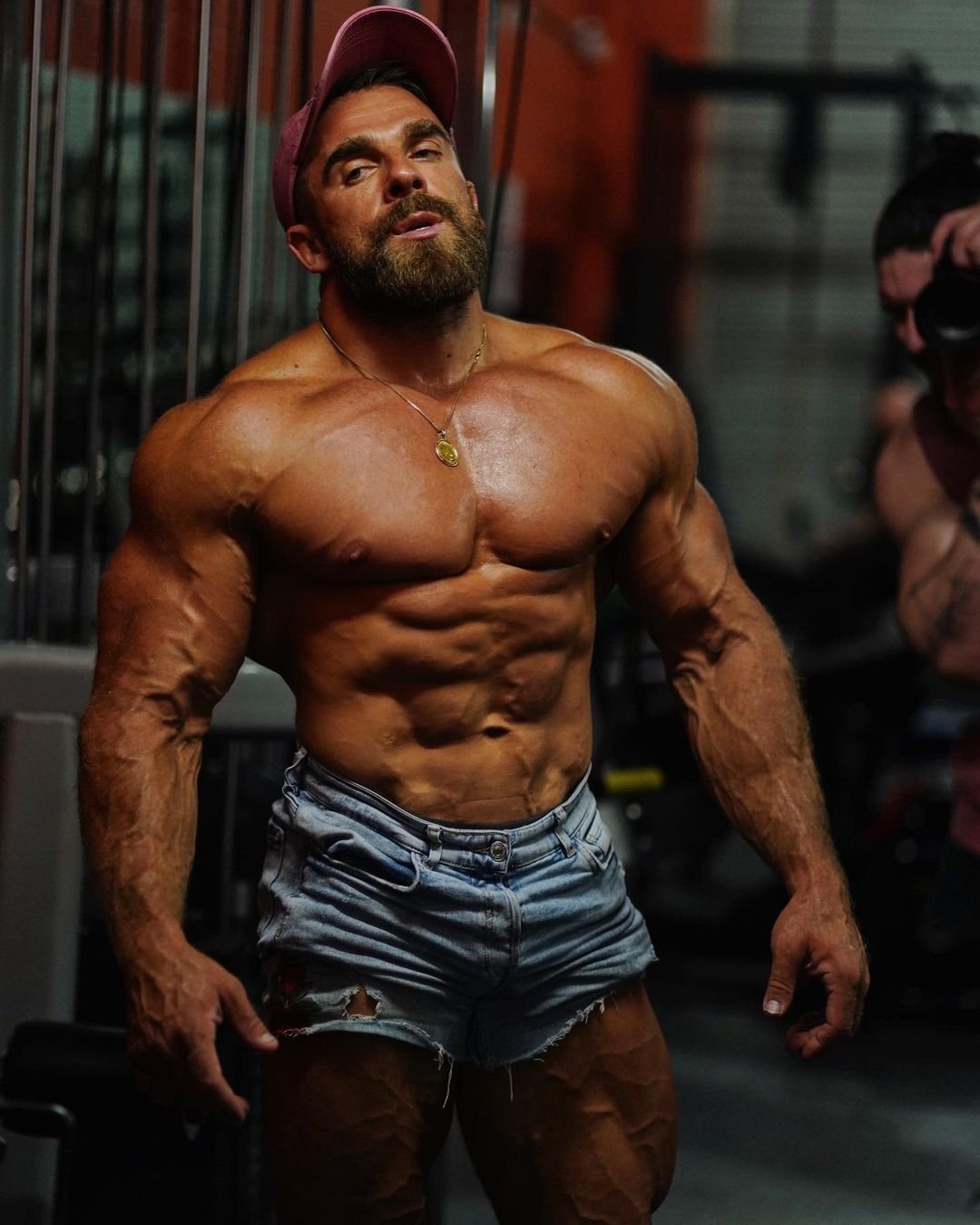 Artemus Dolgin in the gym wearing denim shorts and a cap, showing his upper body development