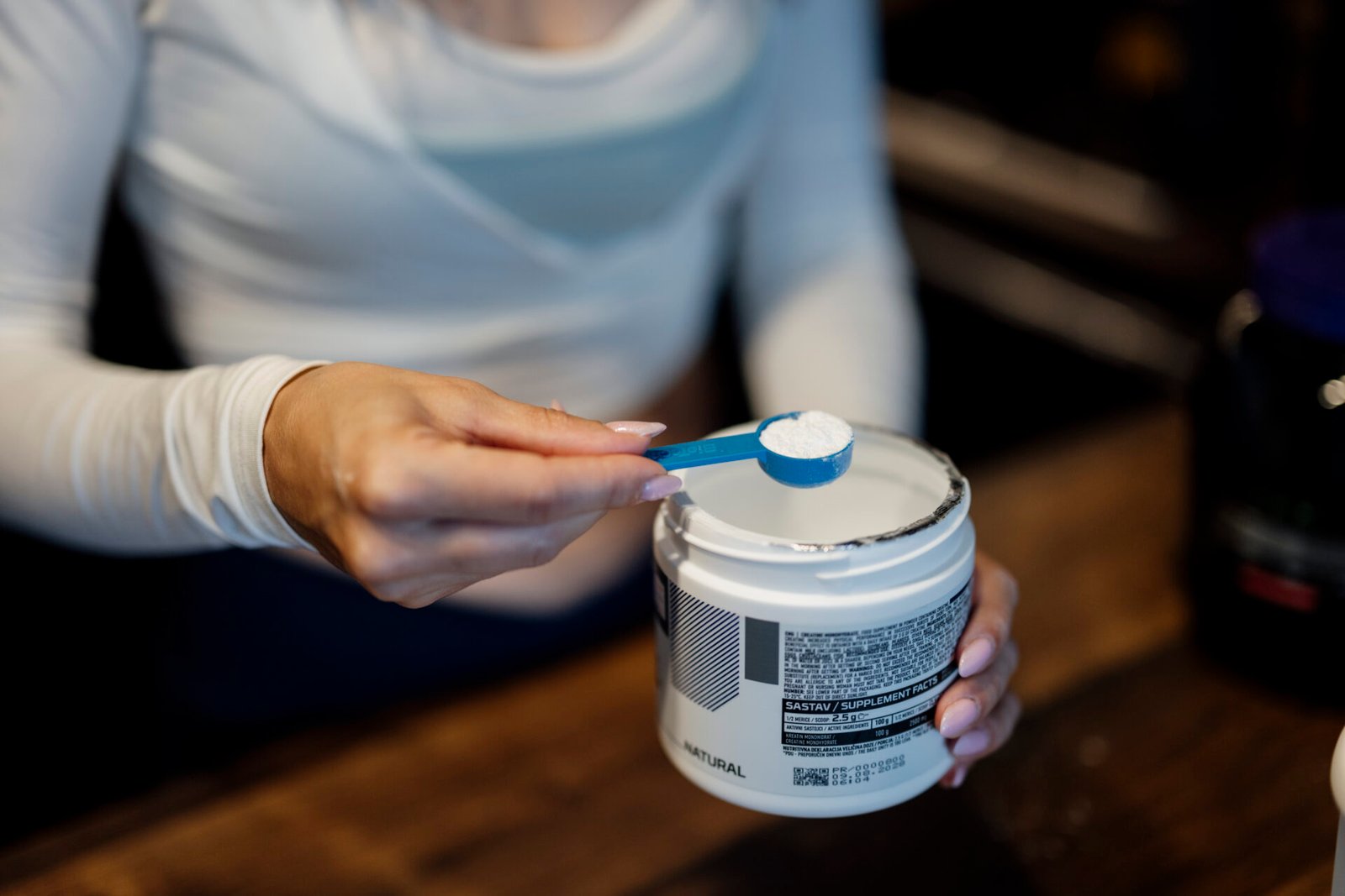 Measuring a scoop of protein powder from a tub in a kitchen