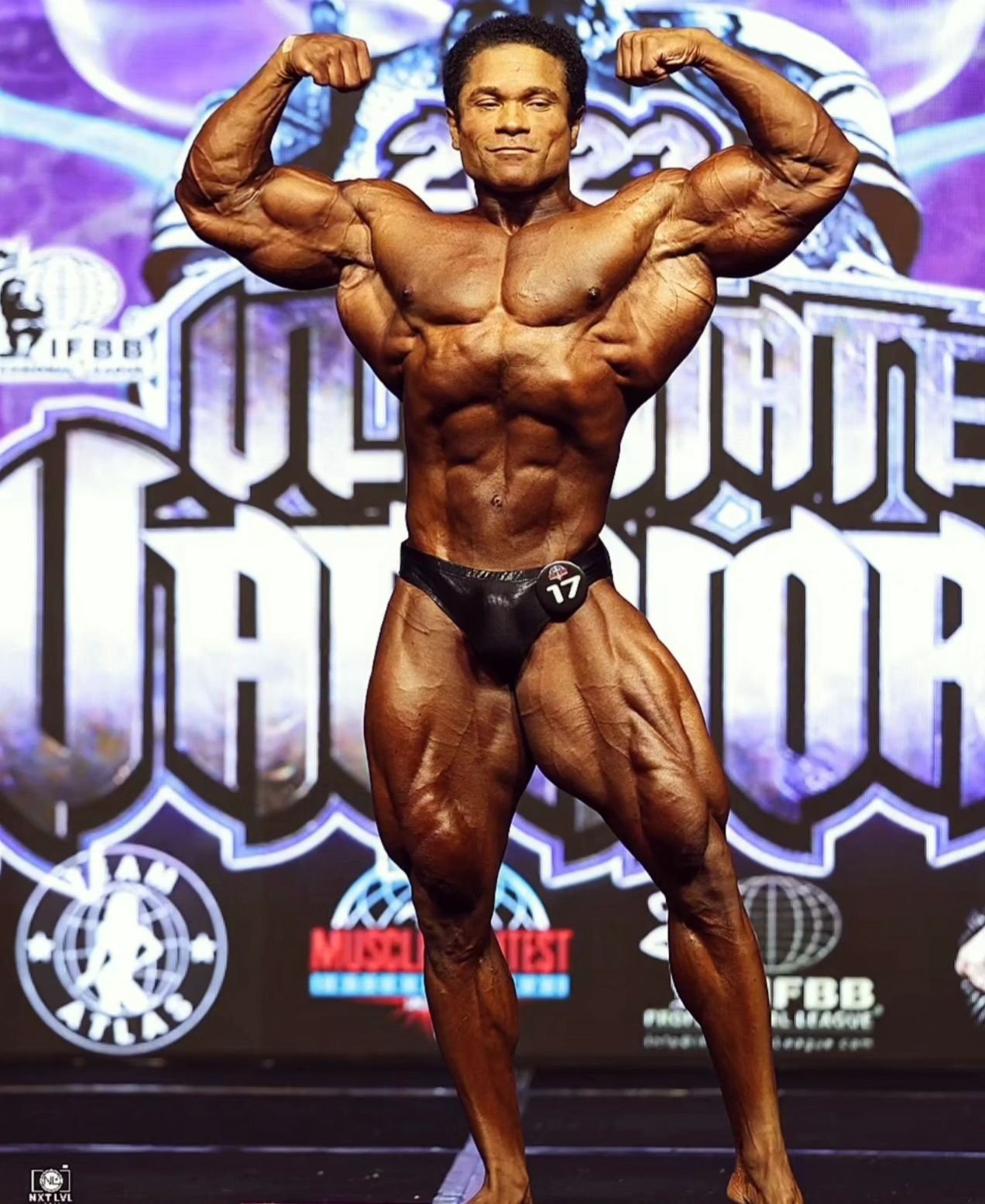Damien Patrick hitting a front double biceps pose on stage at the 2023 Ultimate Warriors Pro