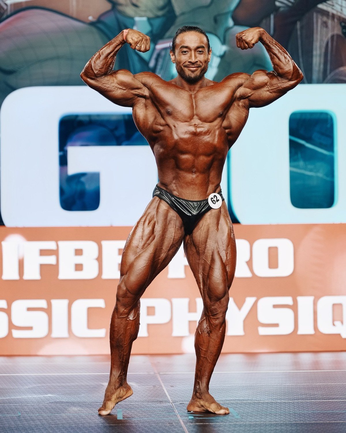 Daryn Shirbayev hitting a front double biceps pose on an IFBB Pro stage