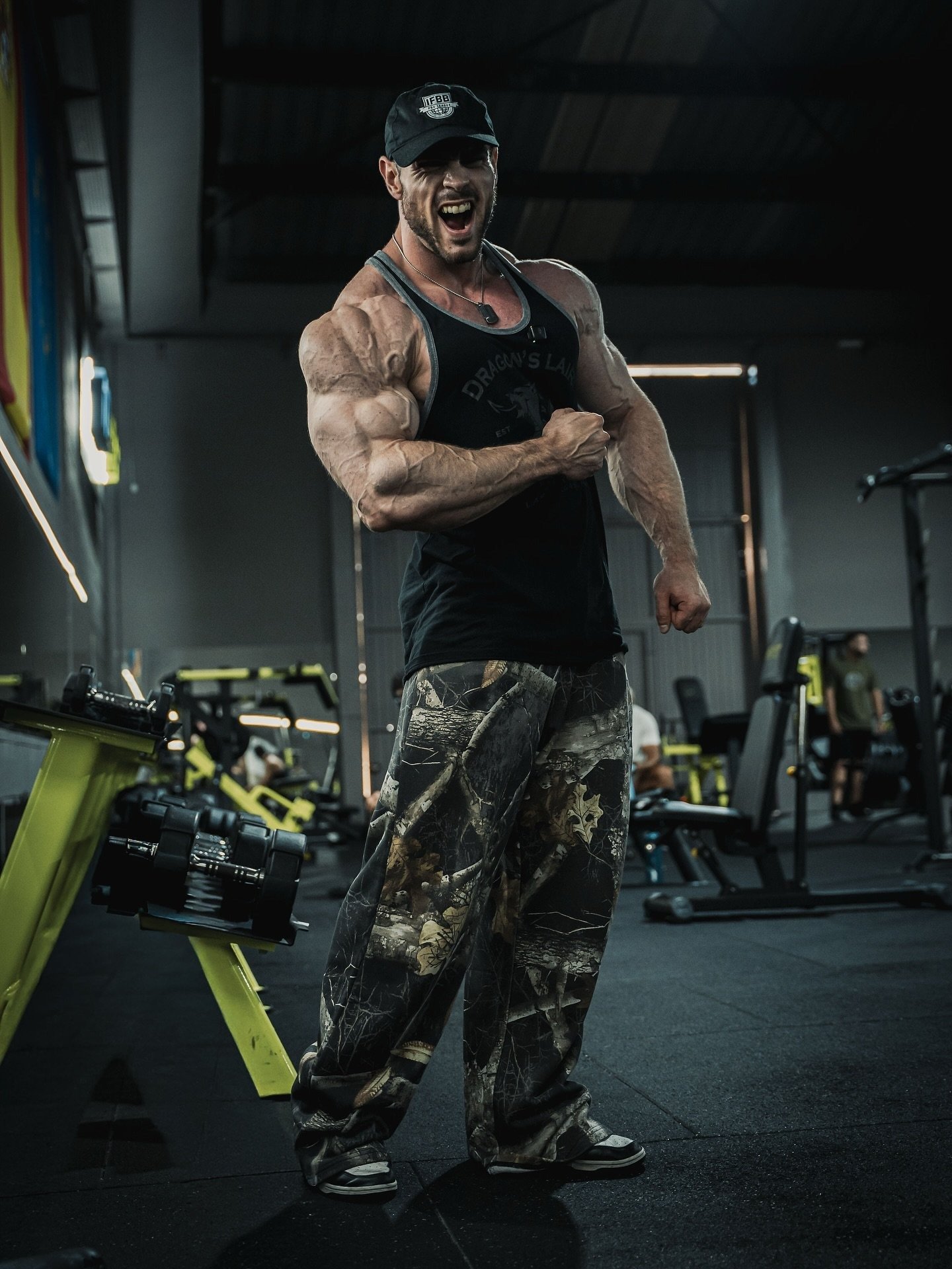 Josema Muñoz flexing during a gym training session wearing an IFBB cap