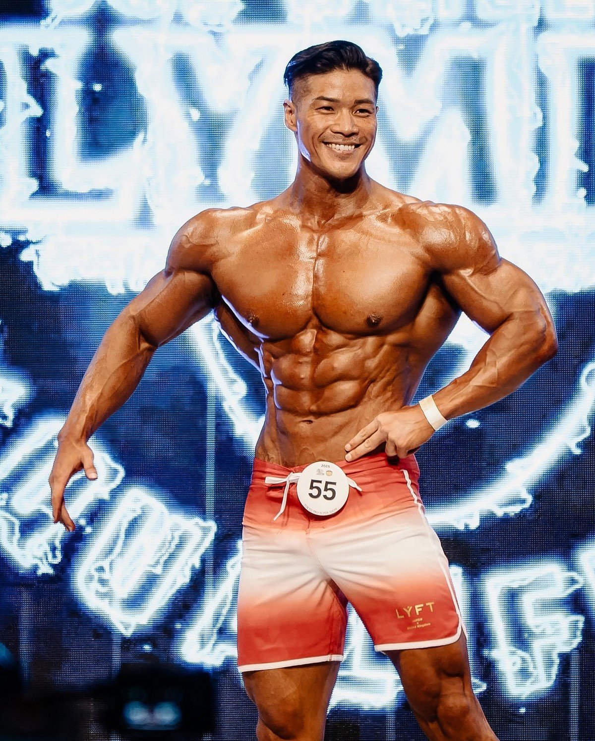 Junpei Taguchi hitting a front pose on stage in red and white LYFT board shorts, competitor number 55