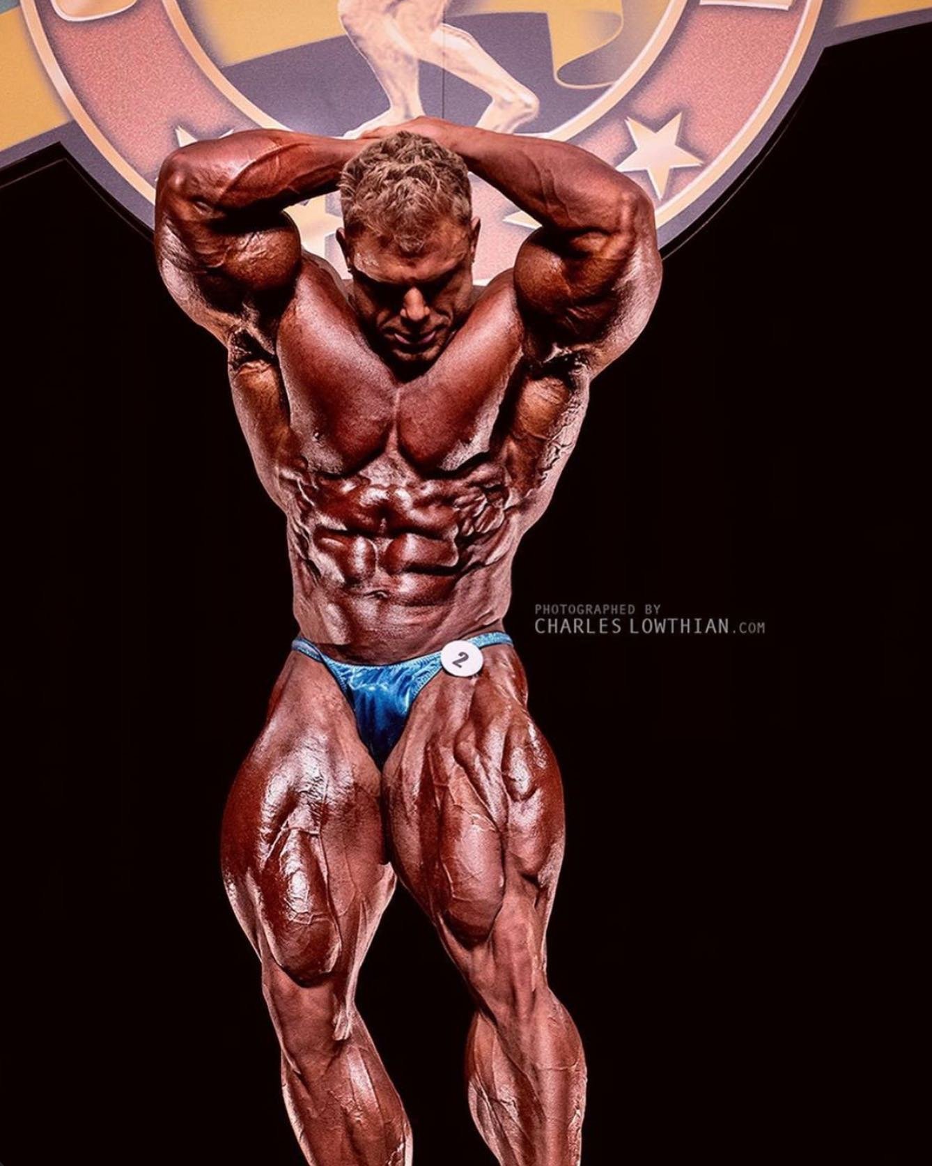 Justin Compton performing an abs and thigh pose on stage in his pro prime