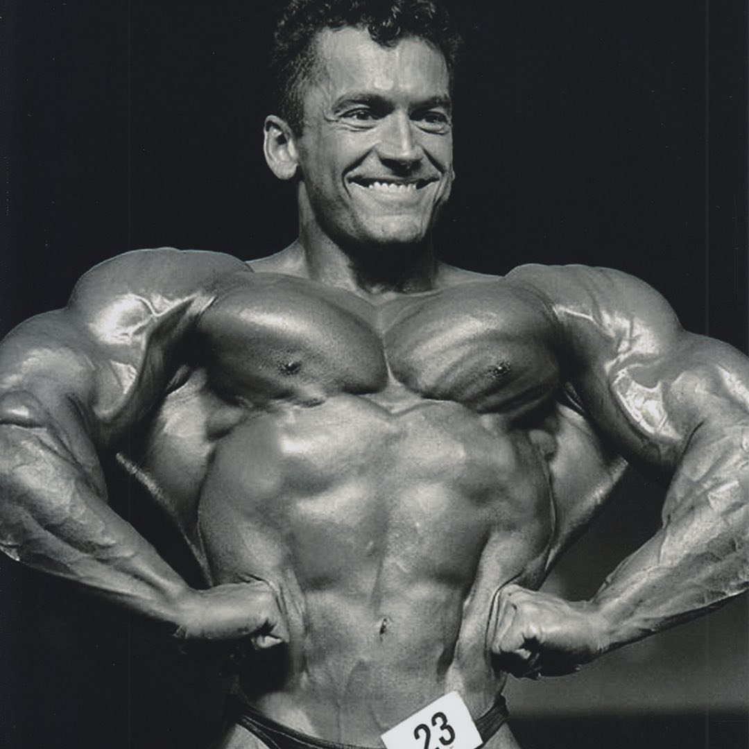 Lee Labrada smiling through a front lat spread on stage during his pro career