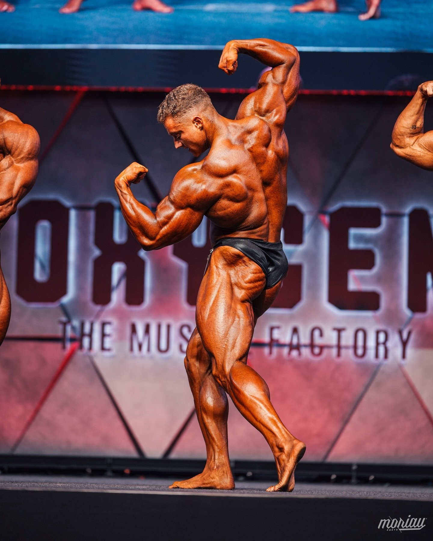 Luca Reger showing his back development in a rear pose on stage