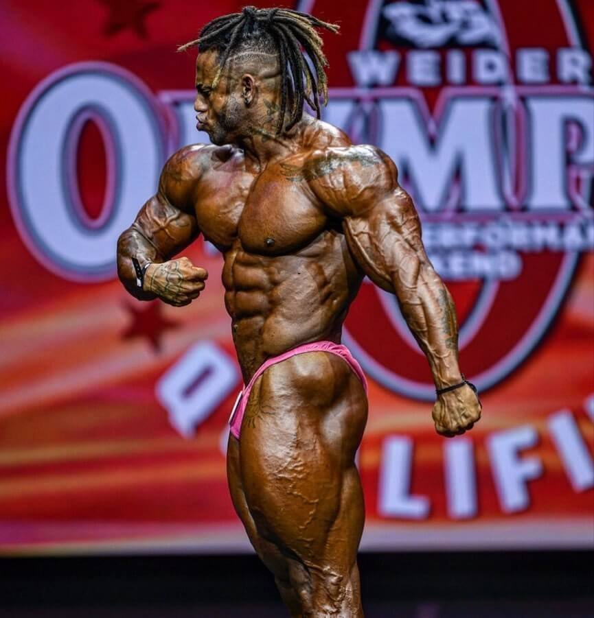Lucas Coelho side pose on an Olympia-branded stage