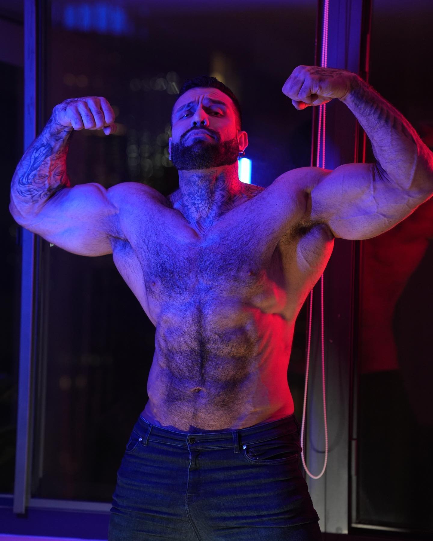 Lukas Lakutsin hitting a front double biceps pose under neon red and blue lights