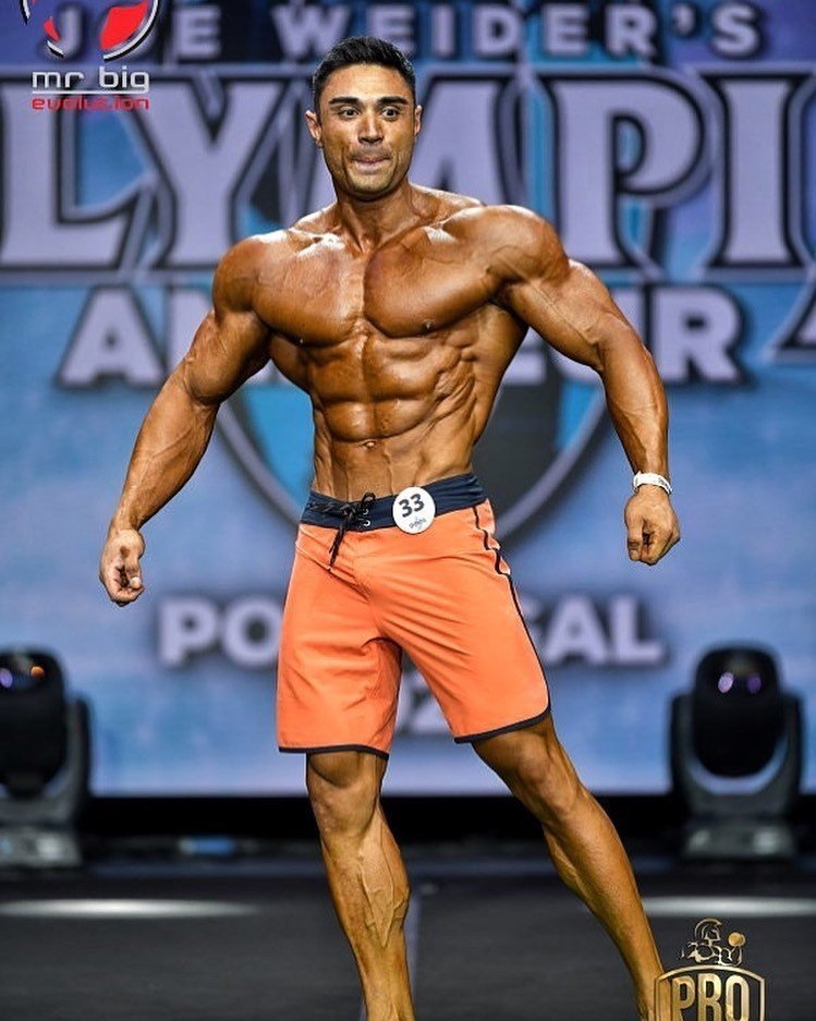 Ozcan Kirant posing on stage at the Olympia Amateur Portugal in orange board shorts