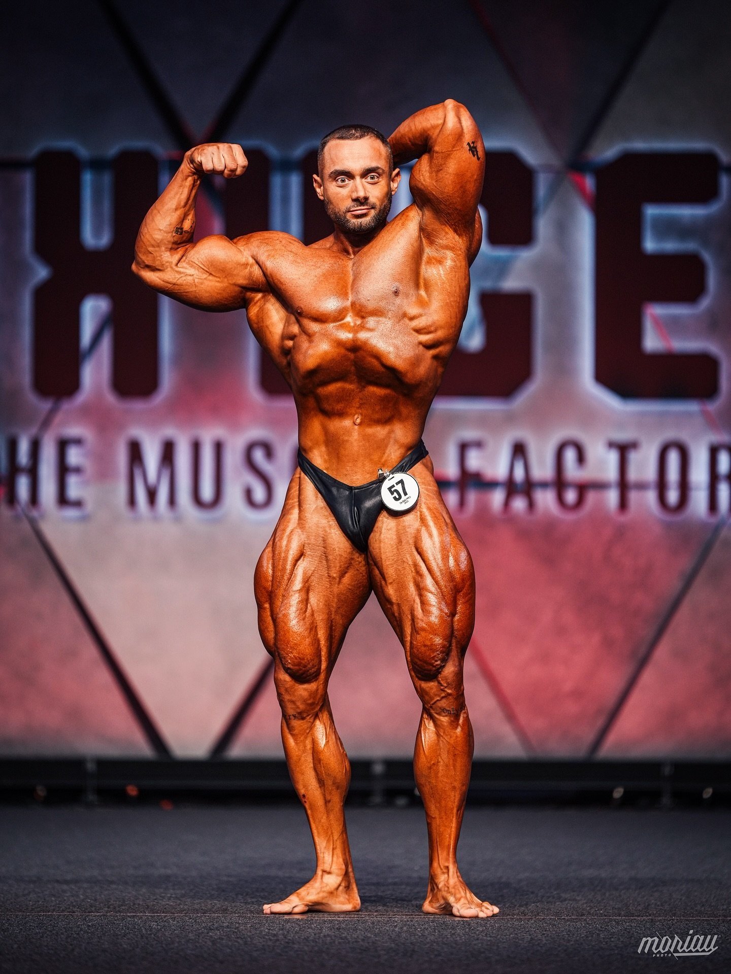 Richard Nagy hitting an abdominal and thigh pose on stage wearing competitor number 57