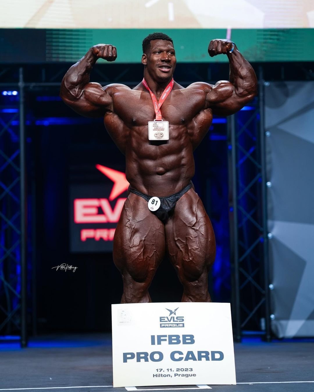 Rubiel Mosquera hitting a front double biceps pose with his medal and IFBB Pro Card sign at EVLS Prague in November 2023