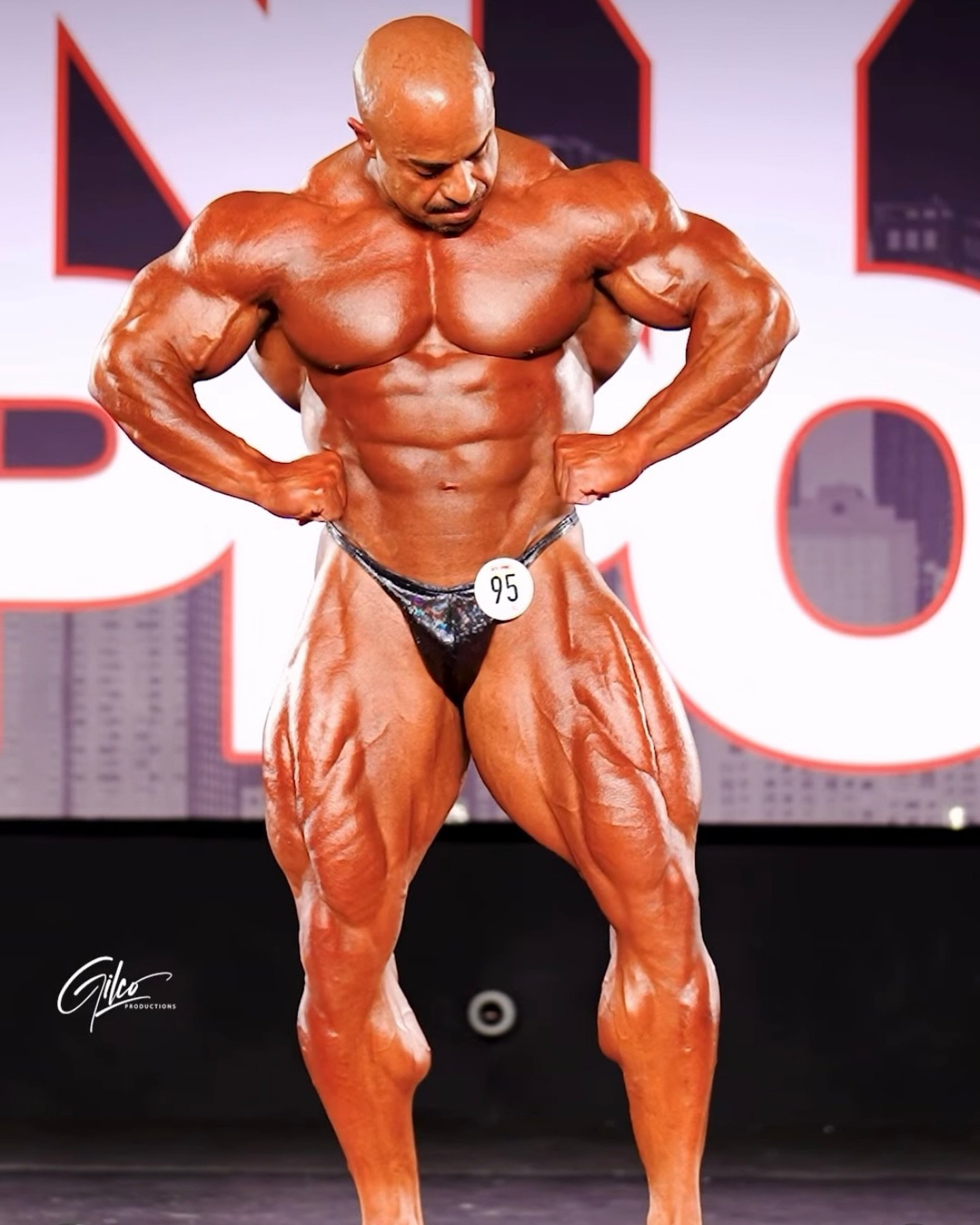 Sasan Heirati performing a front lat spread on stage, showing his wide back and detailed quads