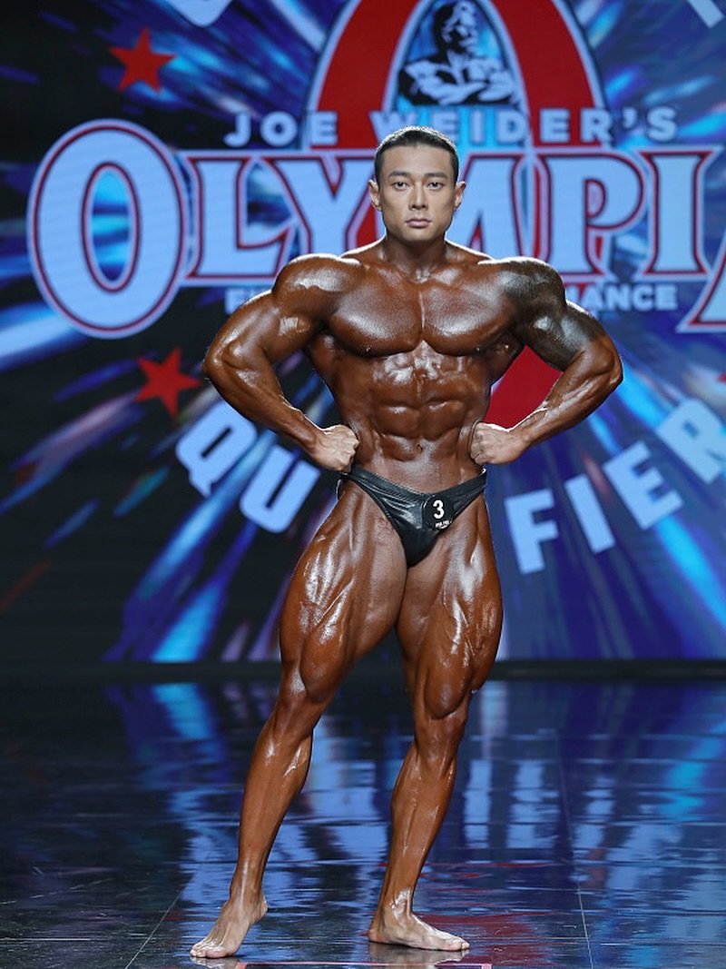 Seonghun Park hitting a front lat spread on a pro stage with an Olympia qualifier backdrop
