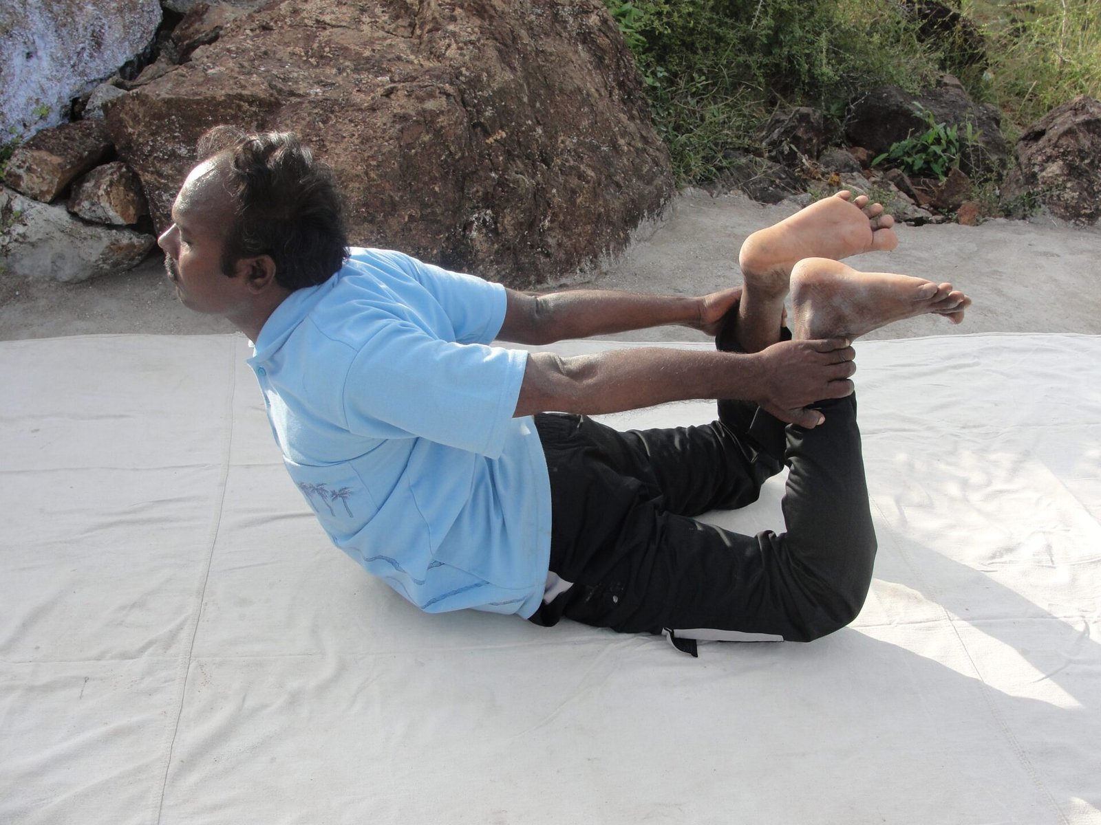 A man lying face down, holding his ankles with his chest lifted in bow pose