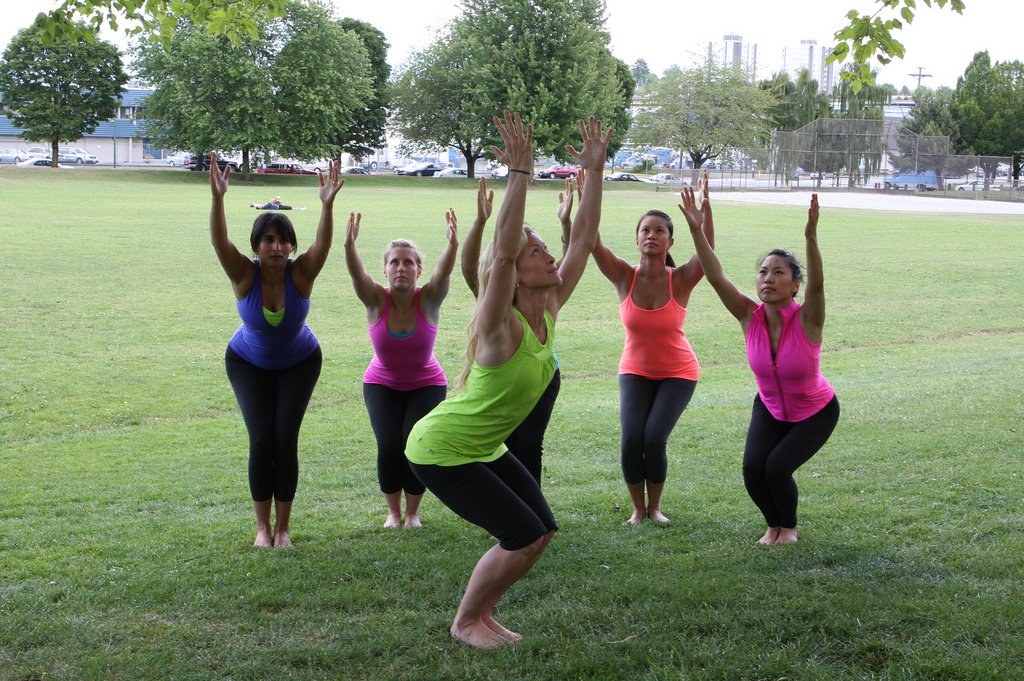 A group outdoors in chair pose, knees bent with arms raised