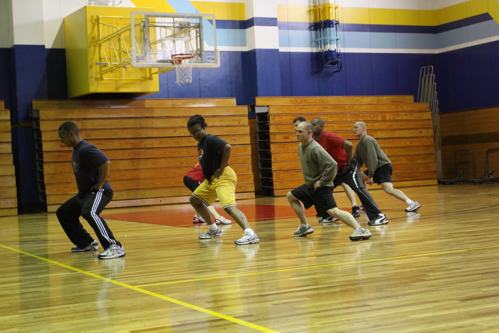 A group in a gym stepping into a side lunge, one leg bent and the other extended to the side