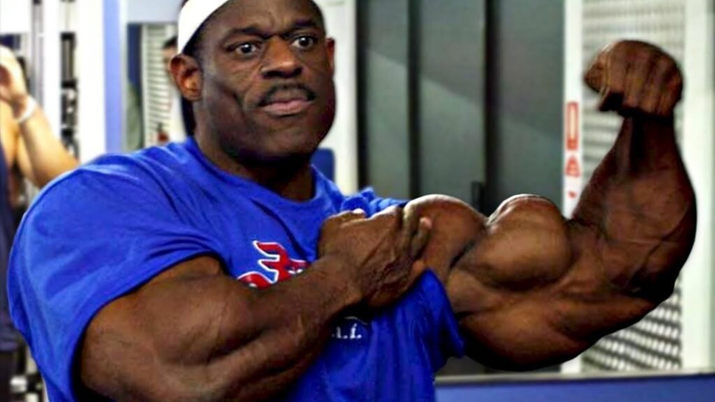 Vince Taylor flexing a biceps in the gym in a blue t-shirt